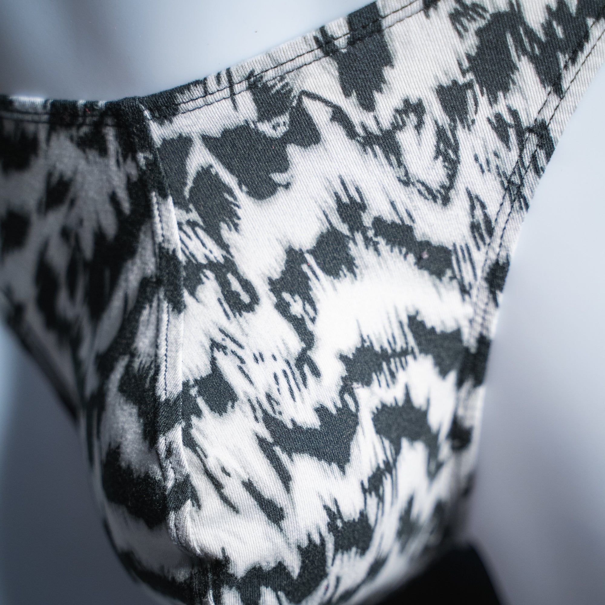 Men's black and white abstract cheetah thong, classic cut, closeup front view.