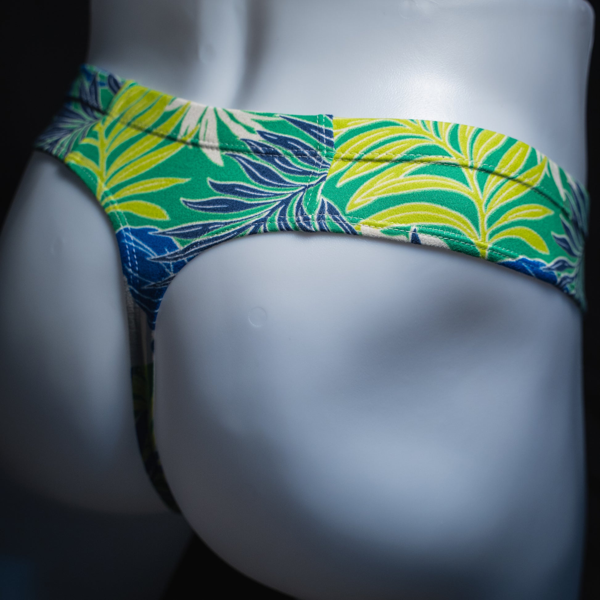 handmade mens thong underwear, green tropical leaves print, soft polyester material, brief cut design, angled back view