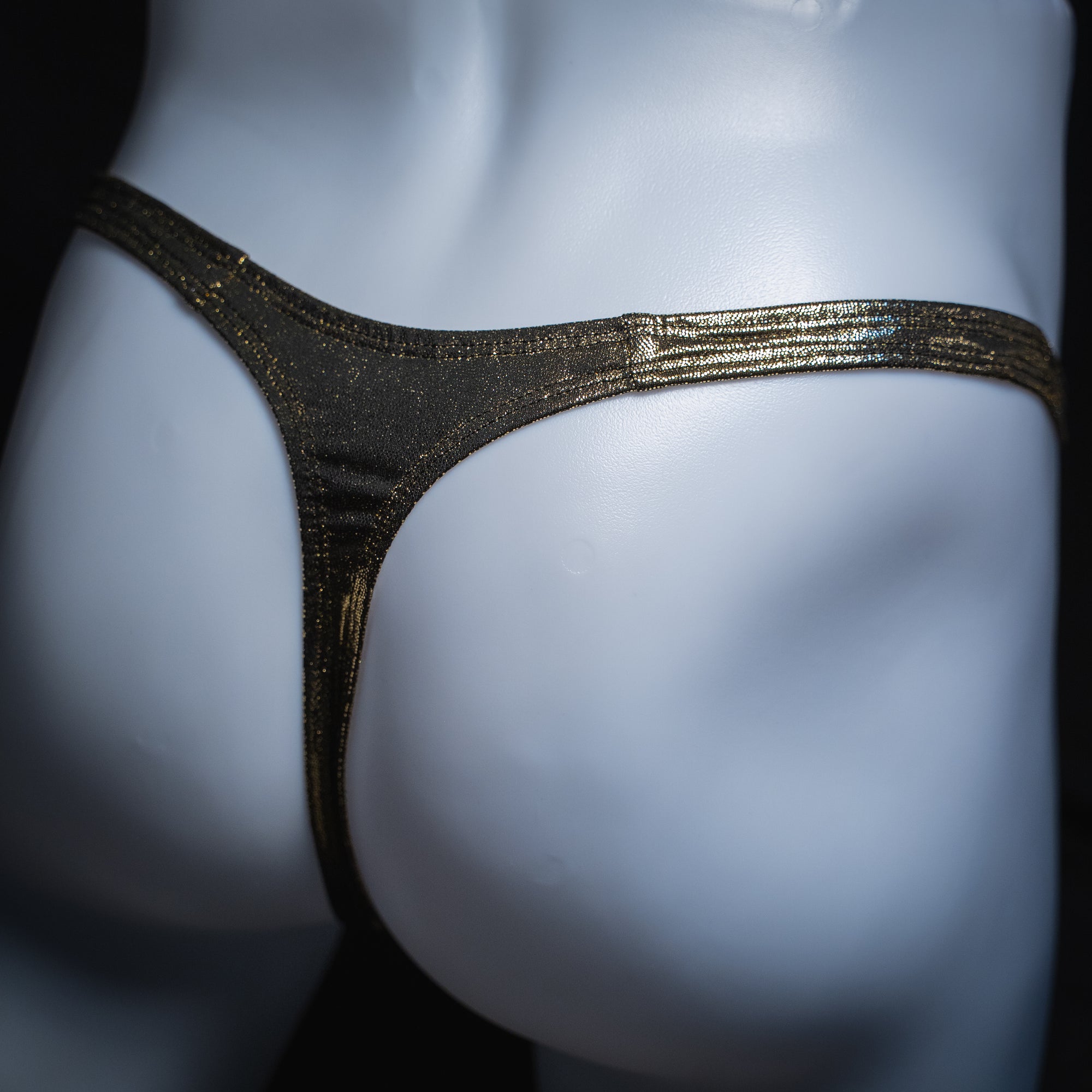 Men's gold metallic thong, slim cut, angled rear view.