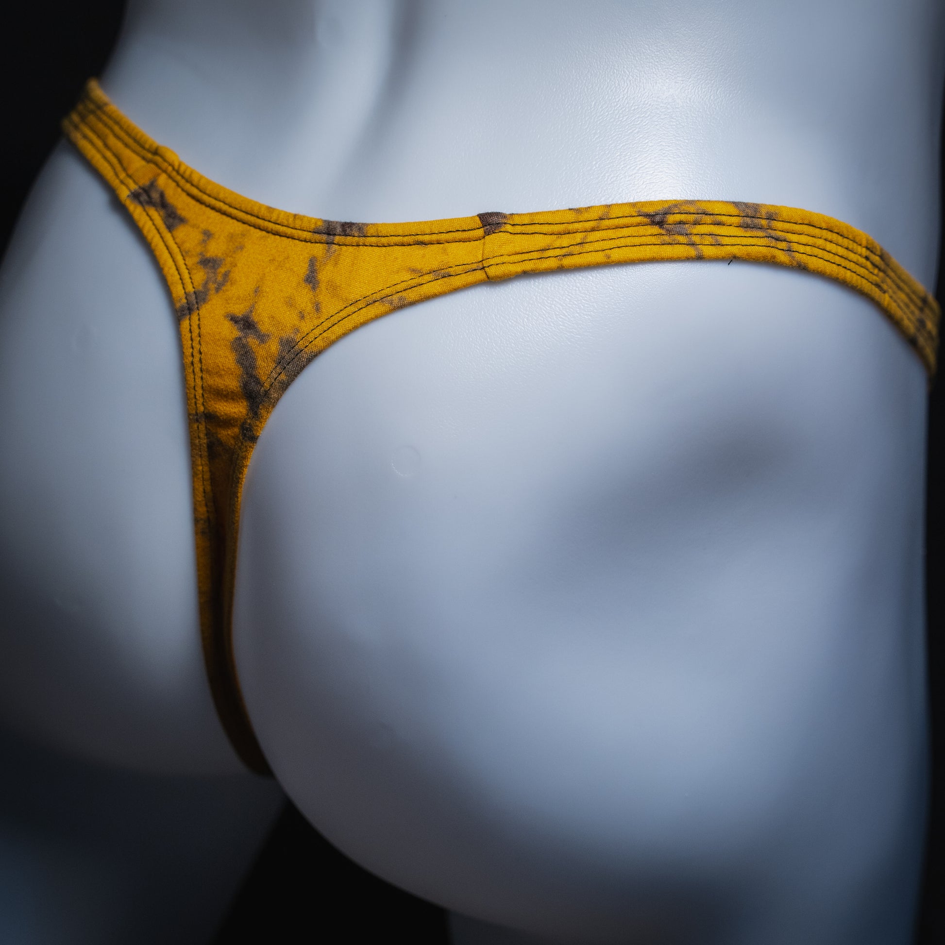 Men's yellow and black tie dye thong, classic cut, angled rear view.