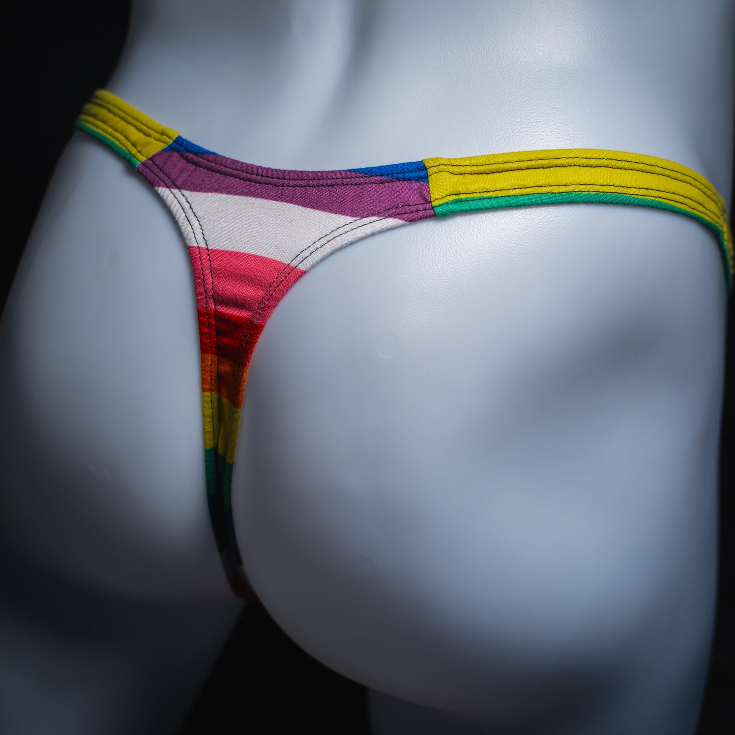 Men's rainbow striped thong underwear, slim cut, angled rear view.