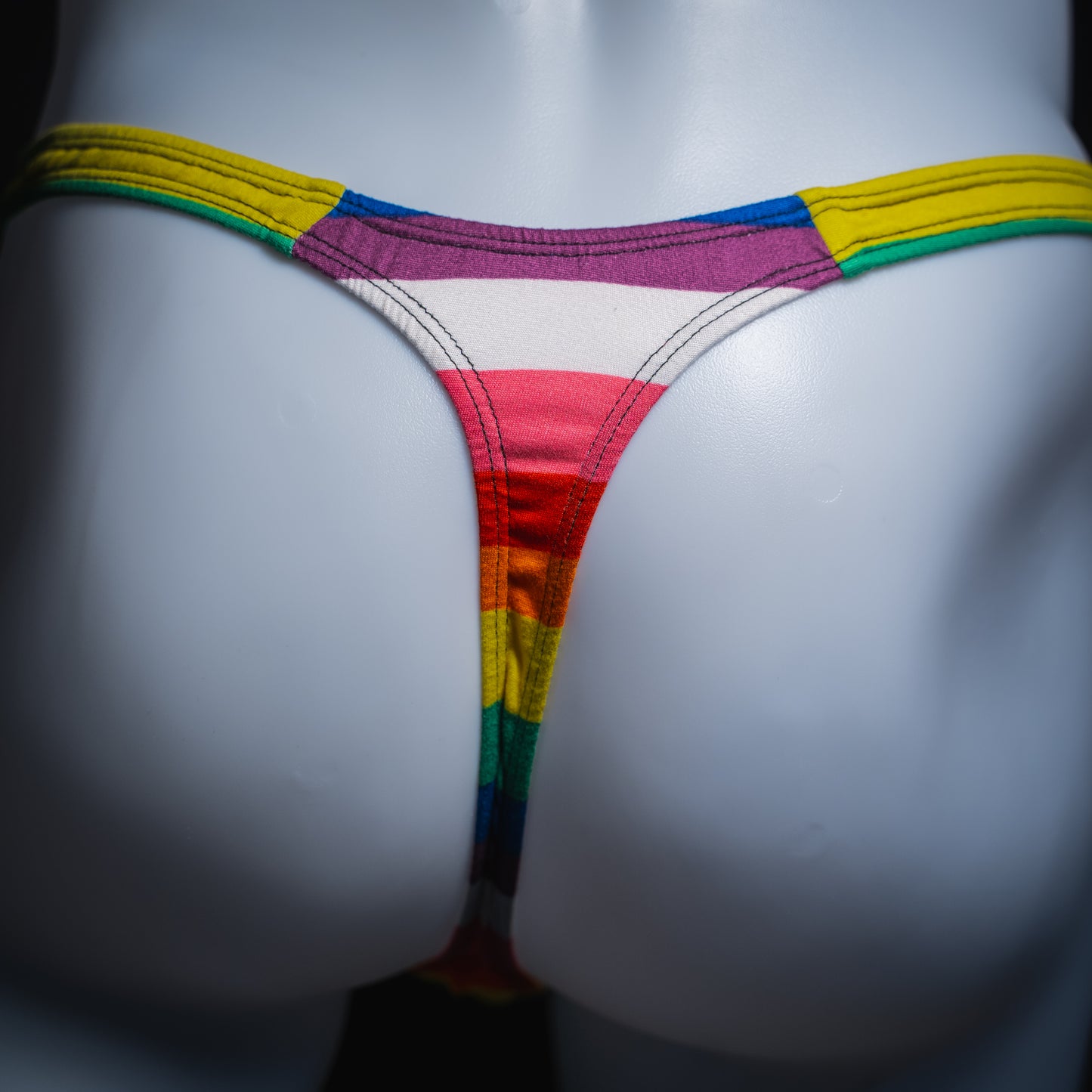 Men's rainbow striped thong underwear, slim cut, rear view.