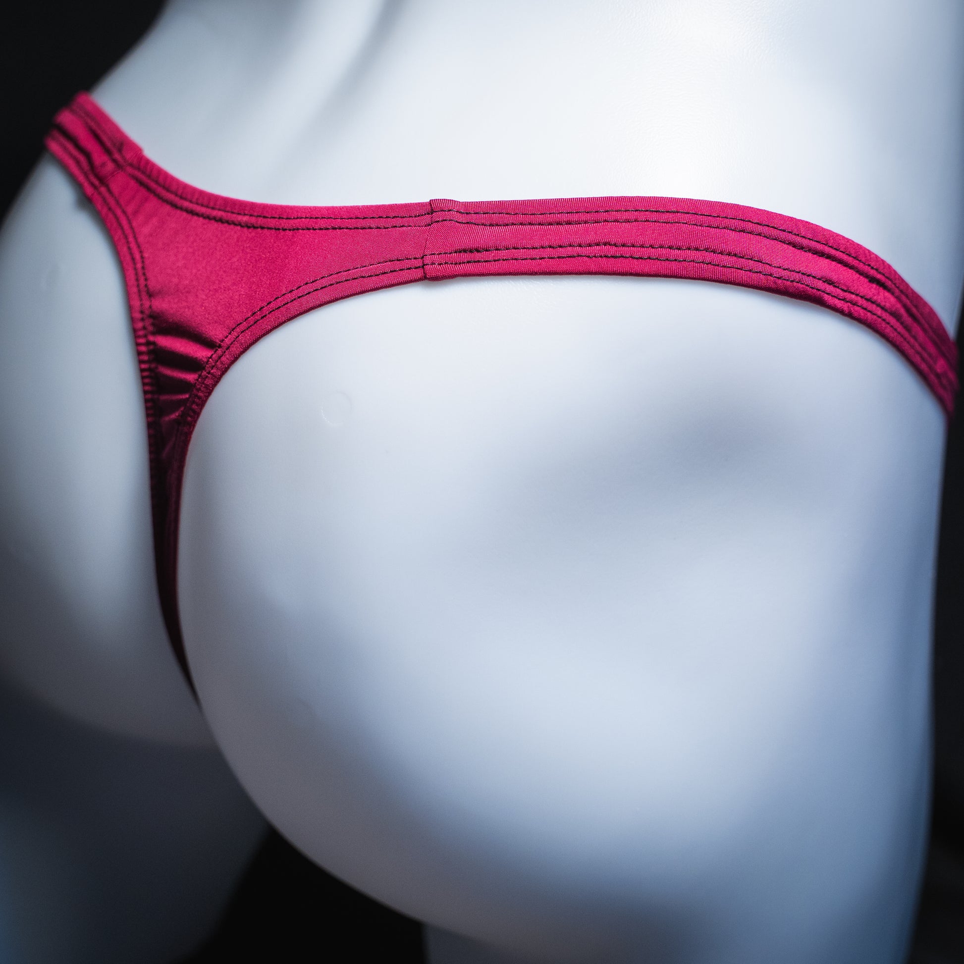 Men's silky maroon thong, classic cut, angled rear view.