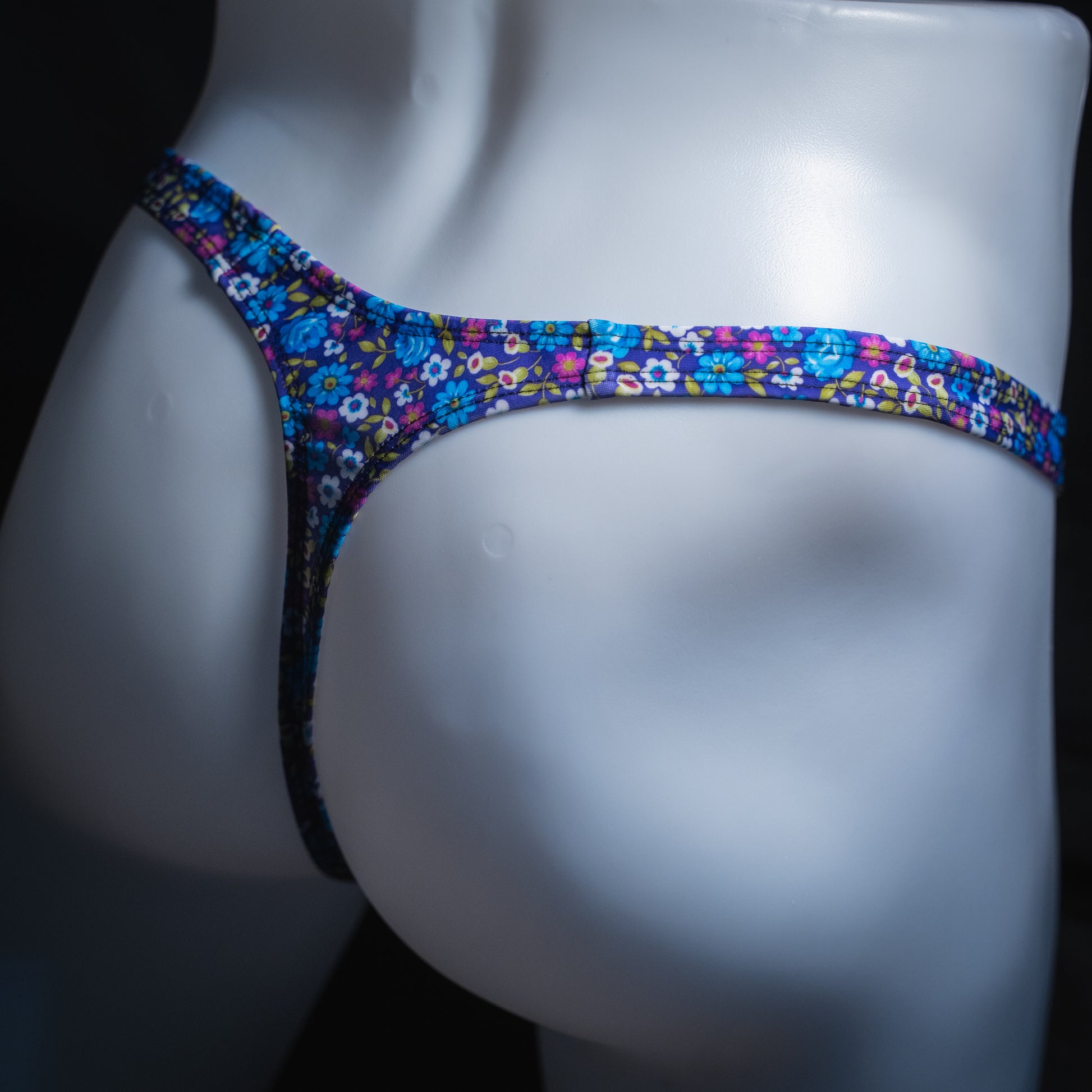 Men's purple and blue floral thong, sim cut, angled rear view.