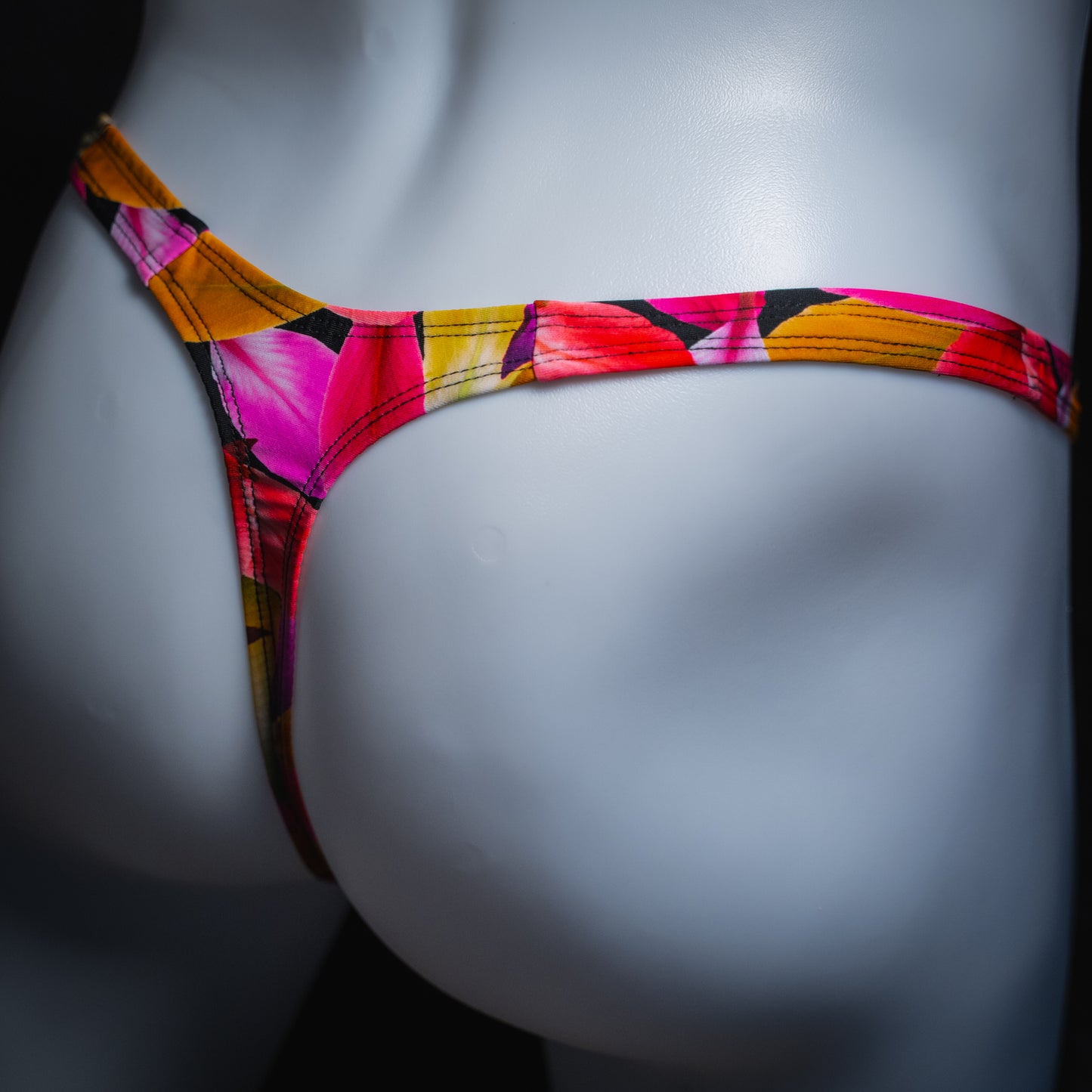 Men's bright floral thong, slim cut, angled rear view.