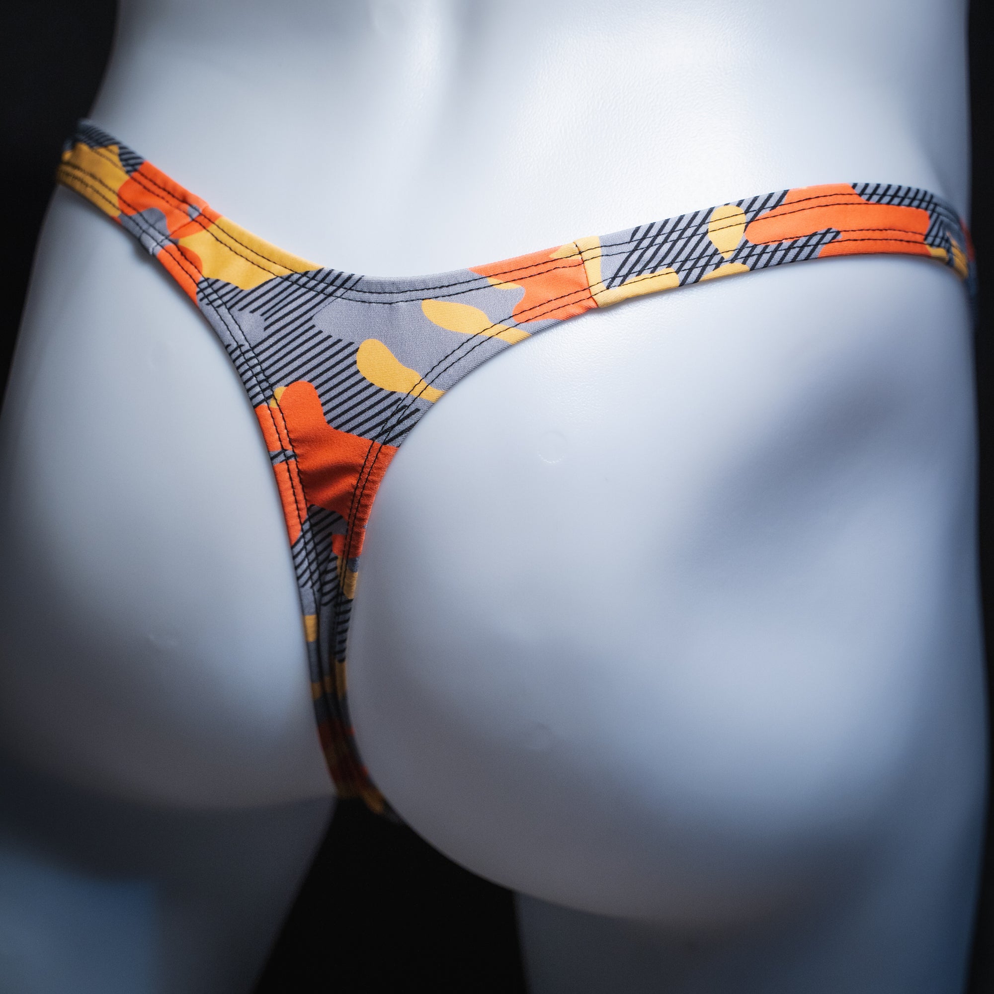Men's orange and gray camo thong, slim cut, angled rear view.