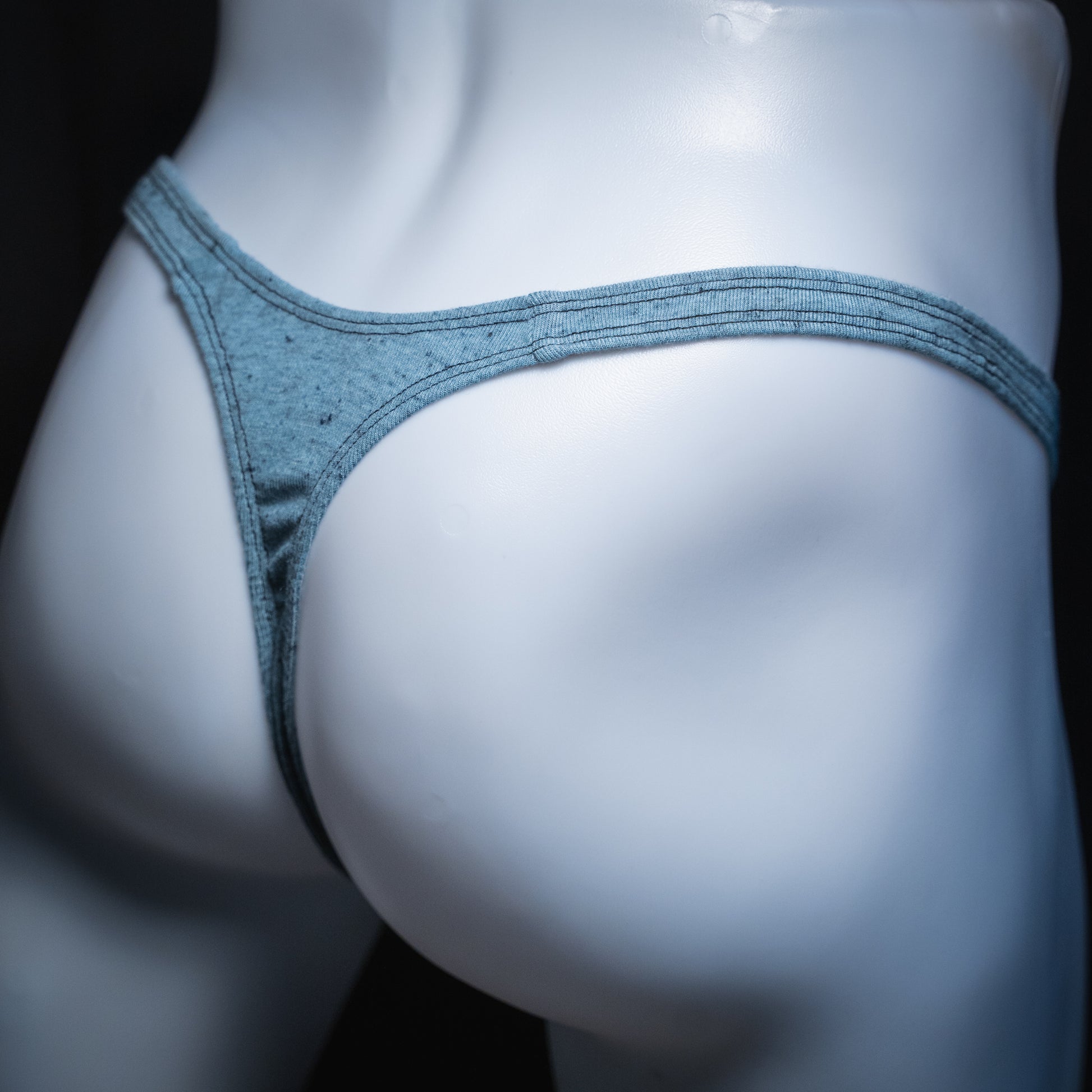 Men's soft blue thong, slim cut, angled rear view.