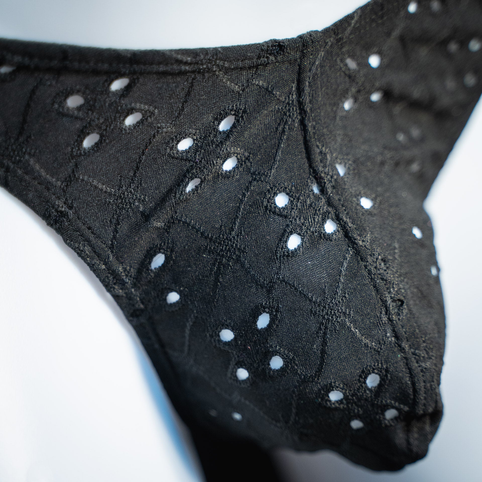handmade mens thong underwear, solid black eyelets, soft polyester material, classic cut variation, closeup angled front view
