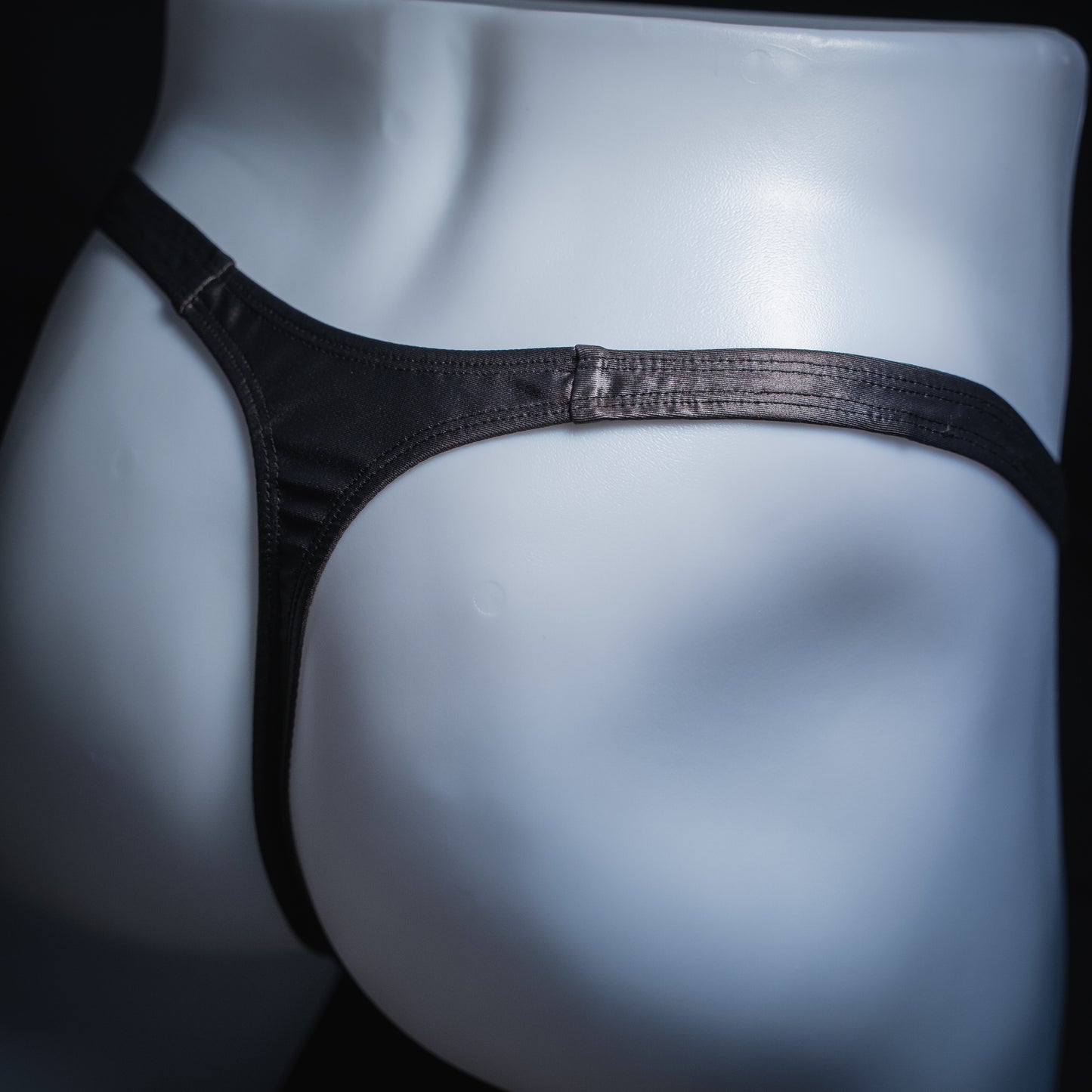 Men's gray wet look thong, classic cut, angled back view.