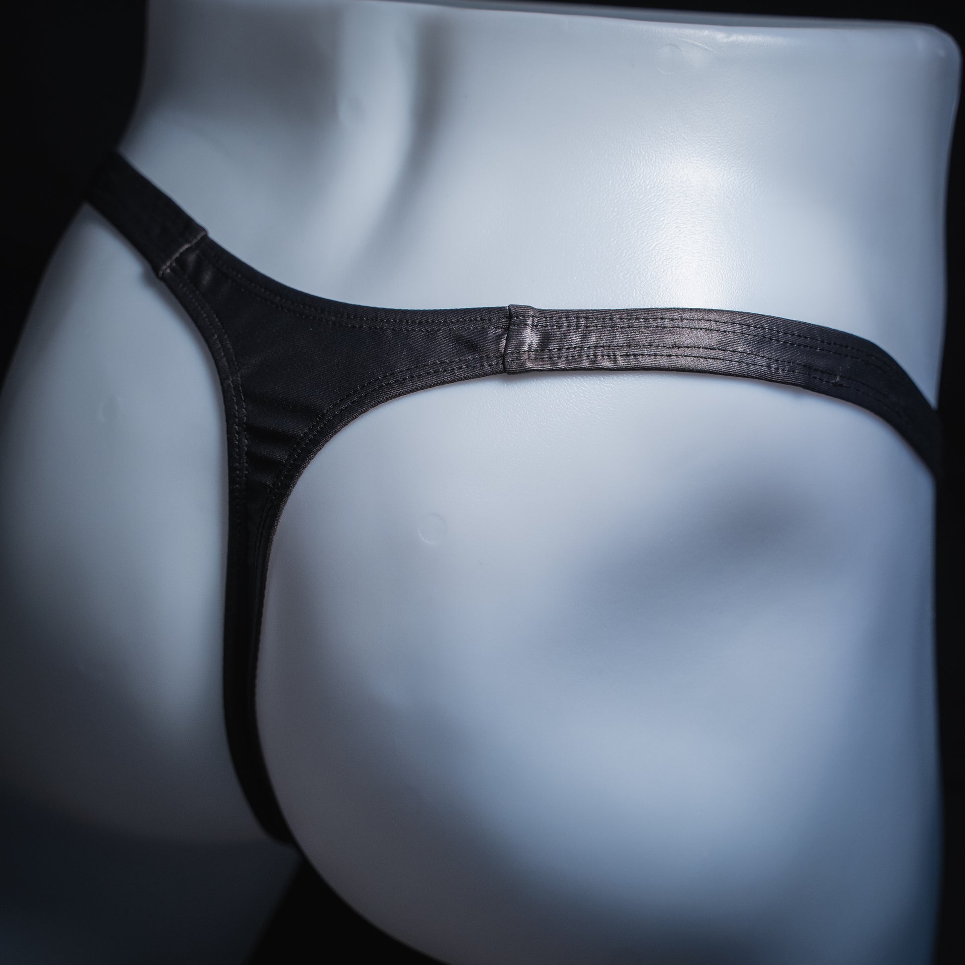 Men's gray wet look thong, classic cut, angled back view.