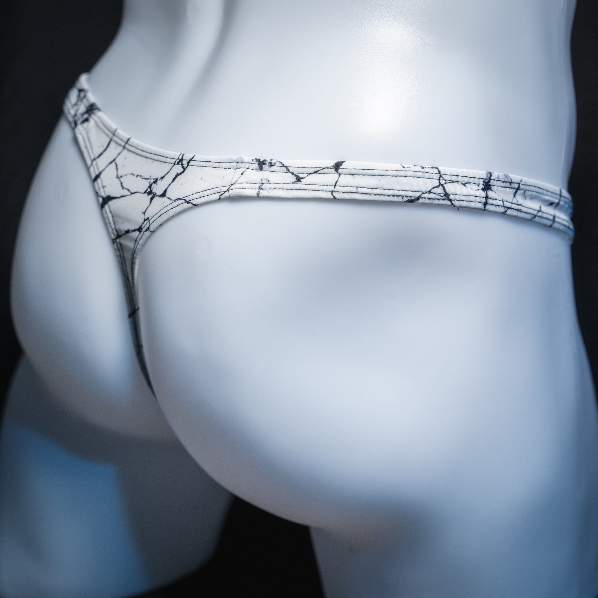 Men's white marble thong, slim cut, angled rear view.